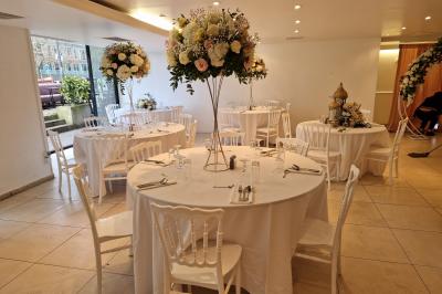 Centre de table floral avec roses et feuillage, entouré de tables dressées dans une salle lumineuse.