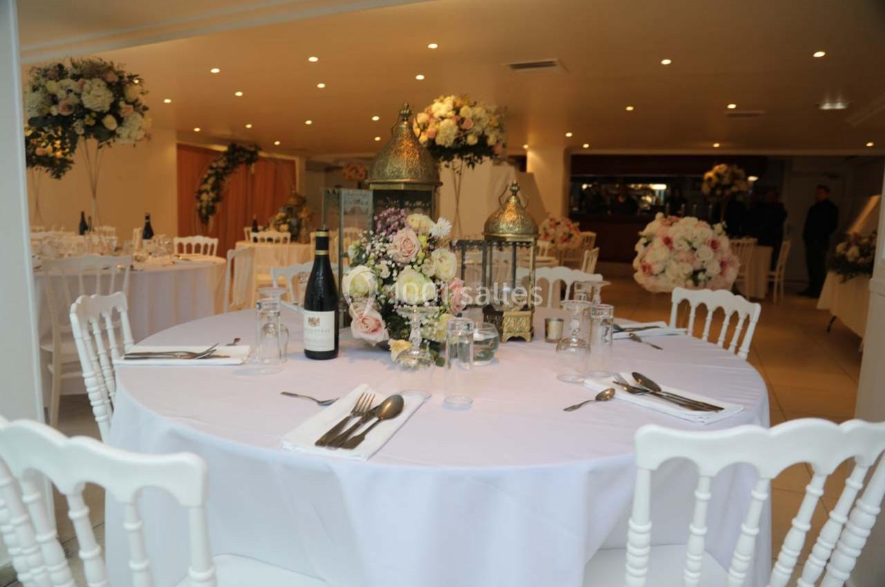 Table ronde décorée avec des fleurs, lanternes dorées, couverts et verres, dans une salle de réception élégante.