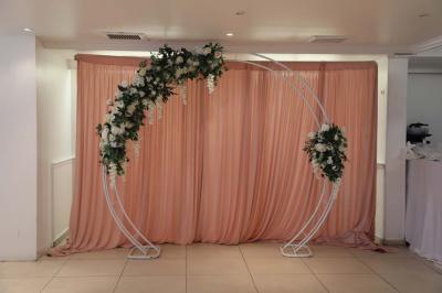 Centre de table floral avec roses et feuillage, entouré de tables dressées dans une salle lumineuse.