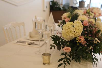 Centre de table floral avec roses et feuillage, entouré de tables dressées dans une salle lumineuse.