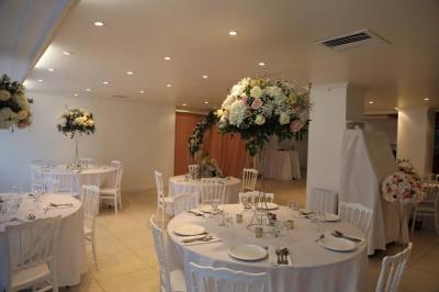 Centre de table floral avec roses et feuillage, entouré de tables dressées dans une salle lumineuse.