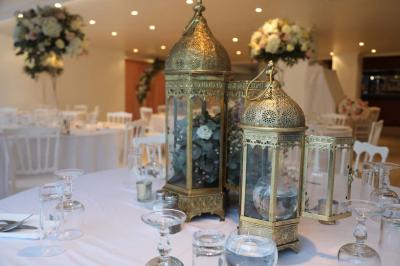 Centre de table floral avec roses et feuillage, entouré de tables dressées dans une salle lumineuse.