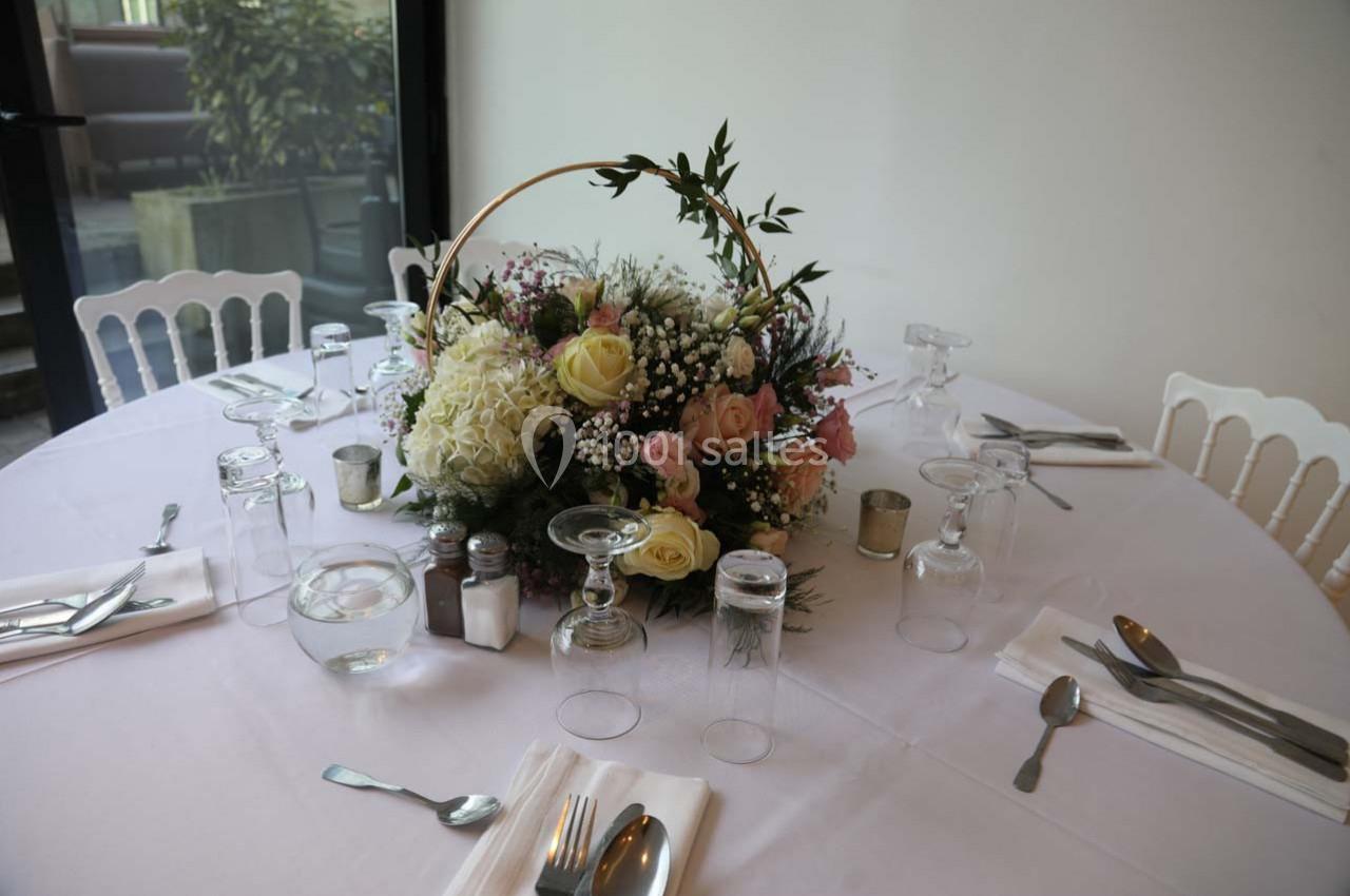 Centre de table floral avec des roses, des hortensias et des feuillages, disposé sur une table dressée avec vaisselle.