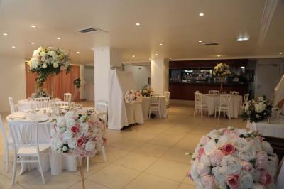Centre de table floral avec roses et feuillage, entouré de tables dressées dans une salle lumineuse.