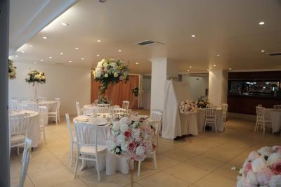 Centre de table floral avec roses et feuillage, entouré de tables dressées dans une salle lumineuse.