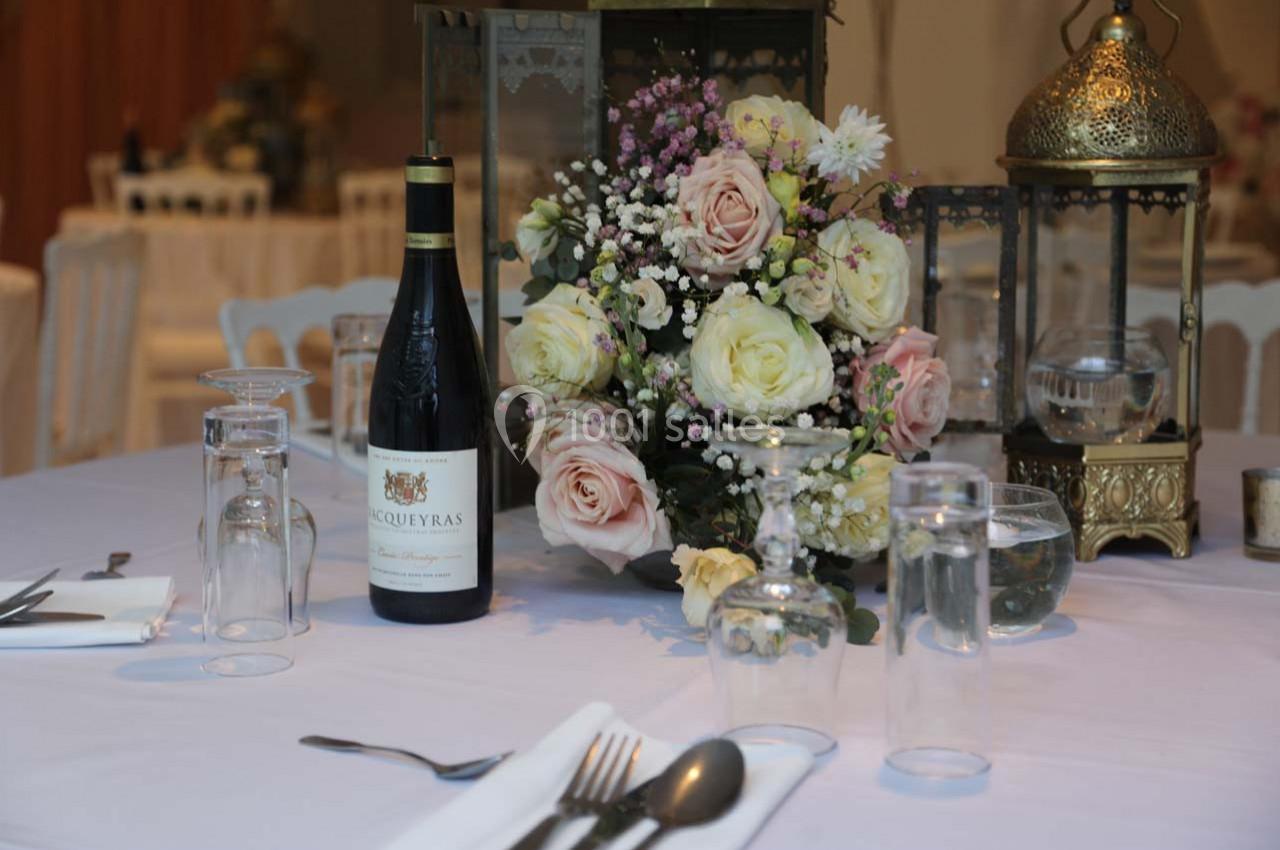 Bouteille de vin, bouquet de fleurs et vaisselle disposés sur une table dressée dans un cadre élégant.