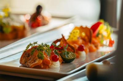 Vue d'une plage avec une terrasse ombragée, des promeneurs, une étendue d'eau et des collines à l'horizon.