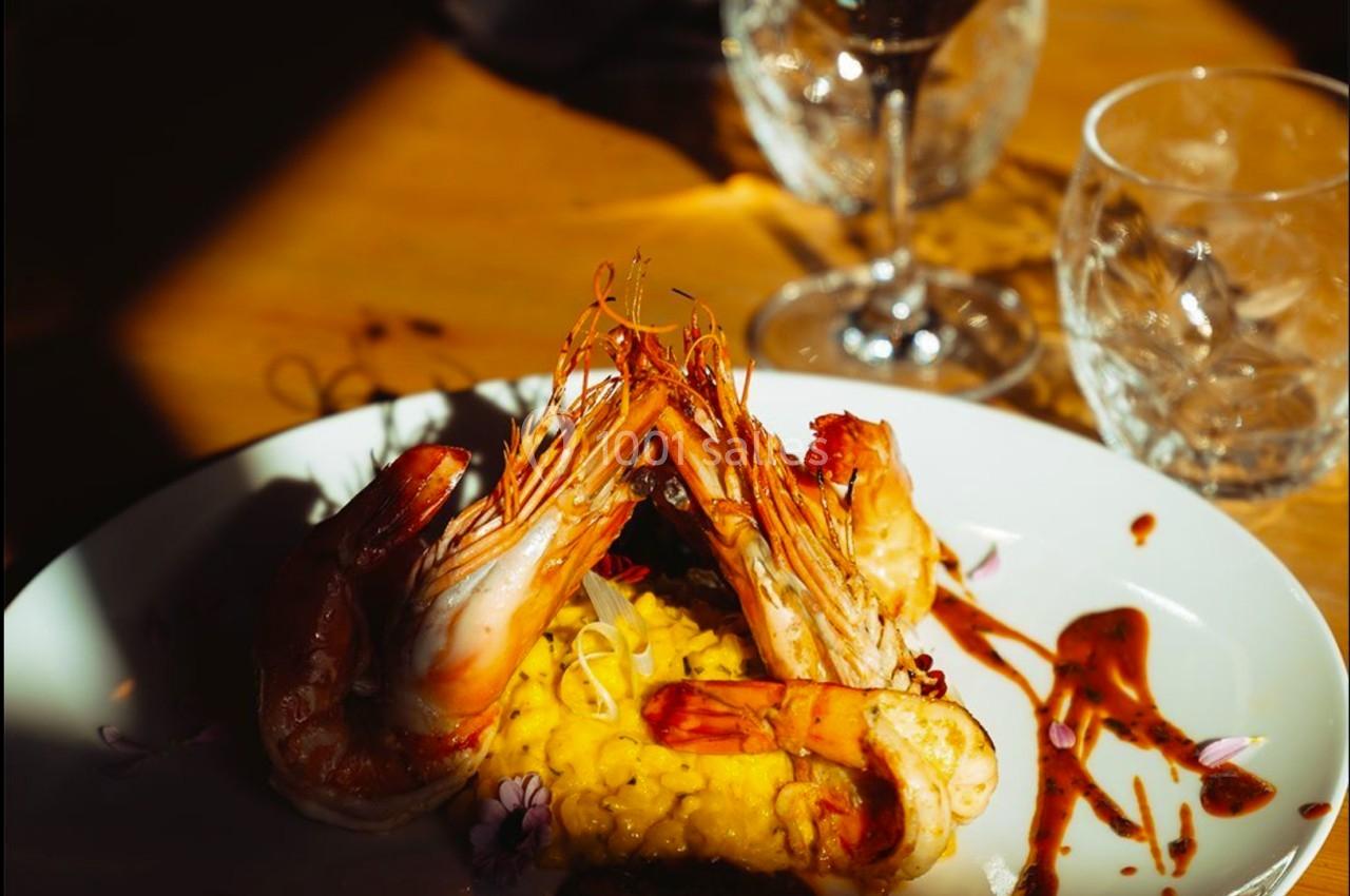 Assiette de risotto au safran avec crevettes grillées, décorée de sauce, servie sur une table en bois avec un verre de vin.