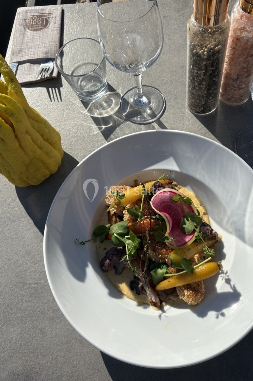 Assiette de légumes colorés et garnitures sur une table avec verres, serviette, citron cèdre et moulins à épices.