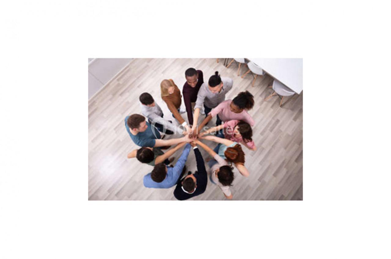 Des personnes debout en cercle joignent leurs mains au centre, symbolisant l'unité et la collaboration.