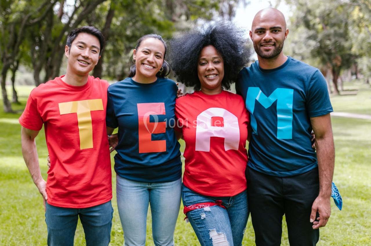 Quatre personnes souriantes portant des t-shirts formant le mot ’TEAM’, debout dans un parc verdoyant.
