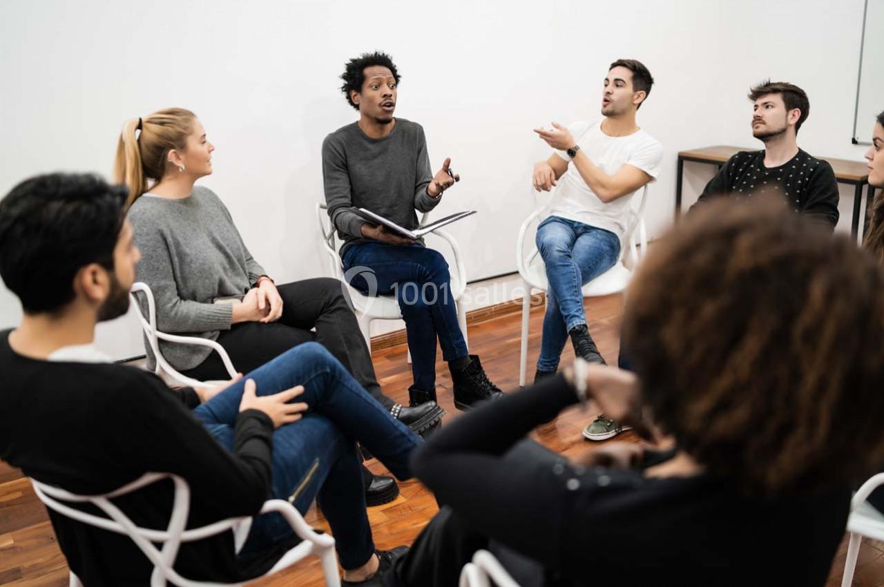 Un groupe de personnes assises en cercle discute dans une salle lumineuse avec un sol en bois.