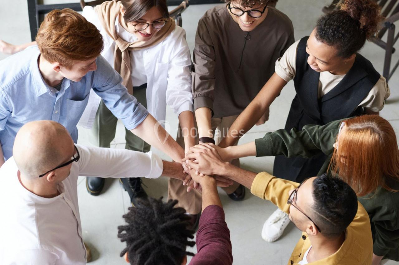 Groupe de personnes debout en cercle, joignant leurs mains au centre dans un geste de collaboration.