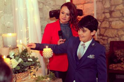 Femme en veste rouge lisant un texte sur un pupitre décoratif, devant un mur en pierre.