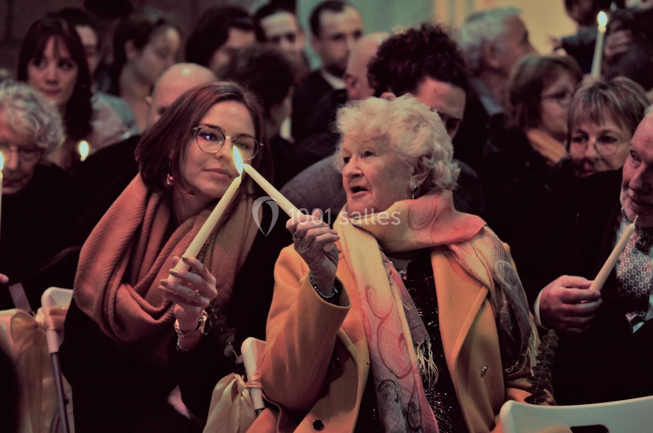 Deux femmes assises côte à côte dans une assemblée, tenant des bougies allumées lors d'un événement.