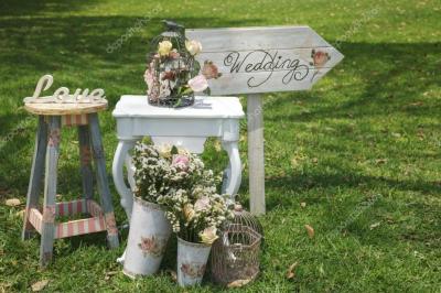 Femme en veste rouge lisant un texte sur un pupitre décoratif, devant un mur en pierre.
