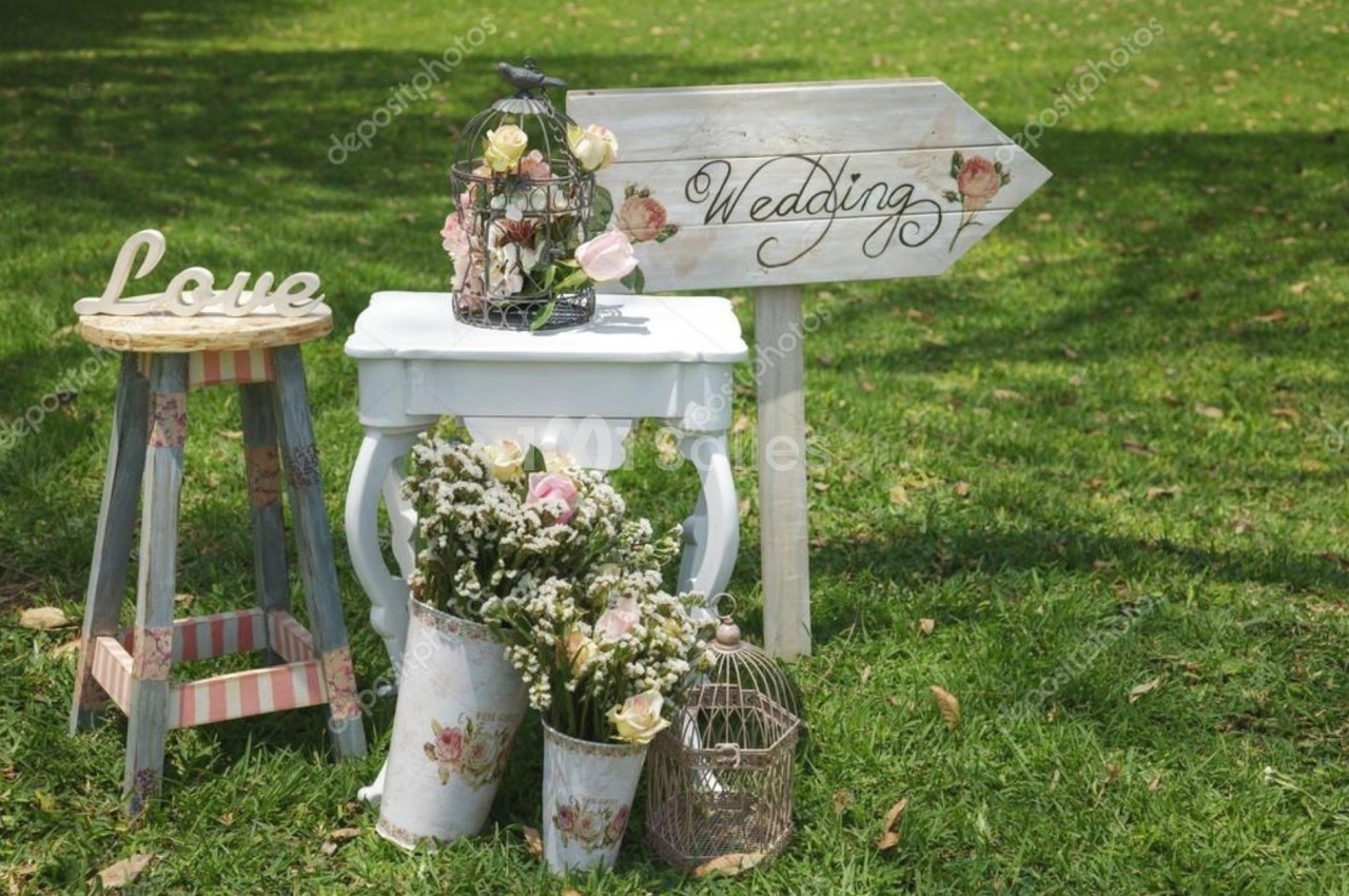 Décoration champêtre avec fleurs, cages à oiseaux et panneau indiquant ’Wedding’ sur une pelouse verte.