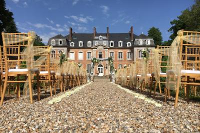 Femme en veste rouge lisant un texte sur un pupitre décoratif, devant un mur en pierre.