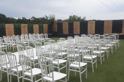 Allée centrale bordée de chaises blanches alignées, installée en extérieur sur une pelouse synthétique.