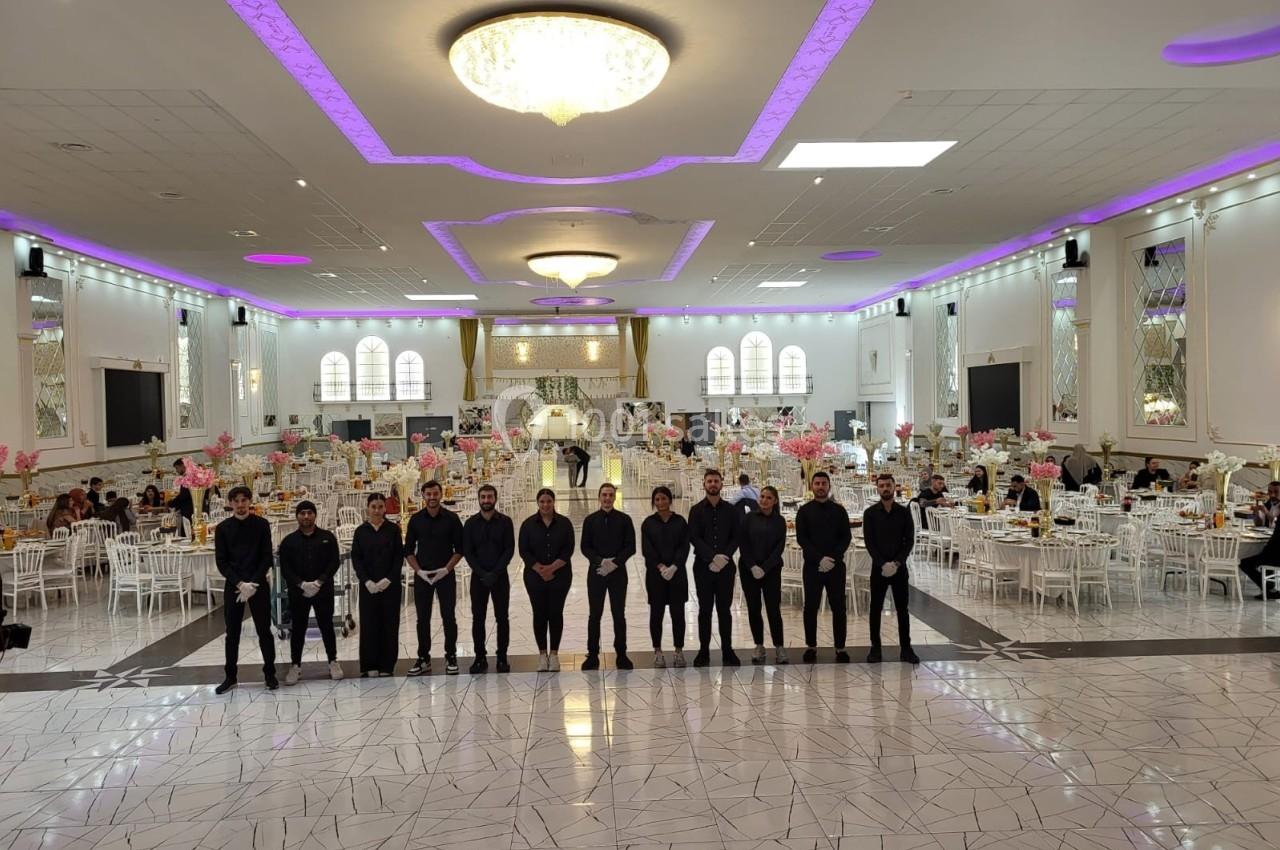 Un groupe de serveurs alignés dans une grande salle de réception décorée avec des tables et des lumières violettes.