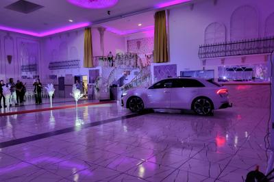 Allée centrale bordée de chaises blanches disposées en extérieur, entourée de panneaux en bois et de murs végétalisés.