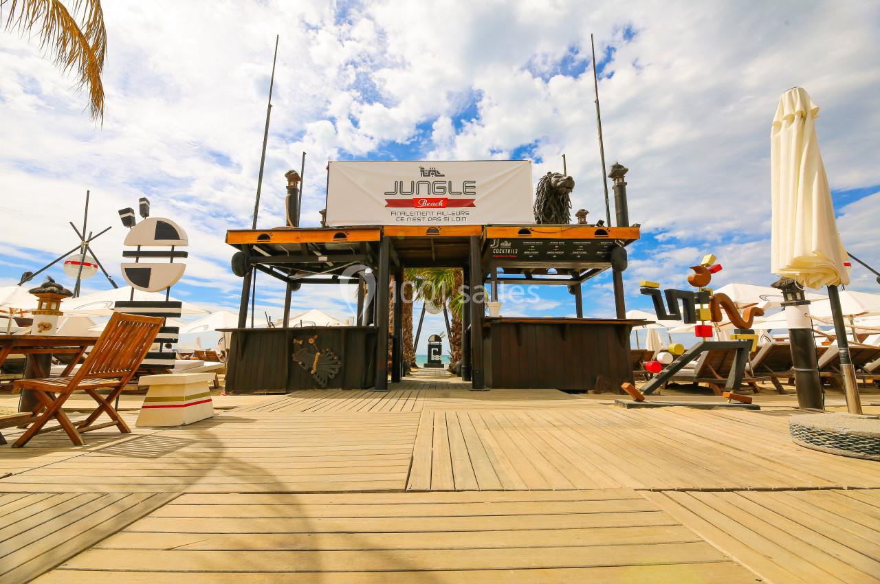 Entrée d'un restaurant de plage en bois avec une enseigne ’Jungle’, entourée de décorations nautiques et parasols.