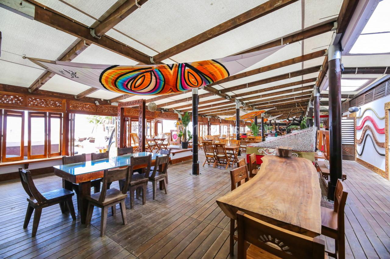 Salle de restaurant en bois avec tables, chaises et décorations colorées sous un toit ouvert.