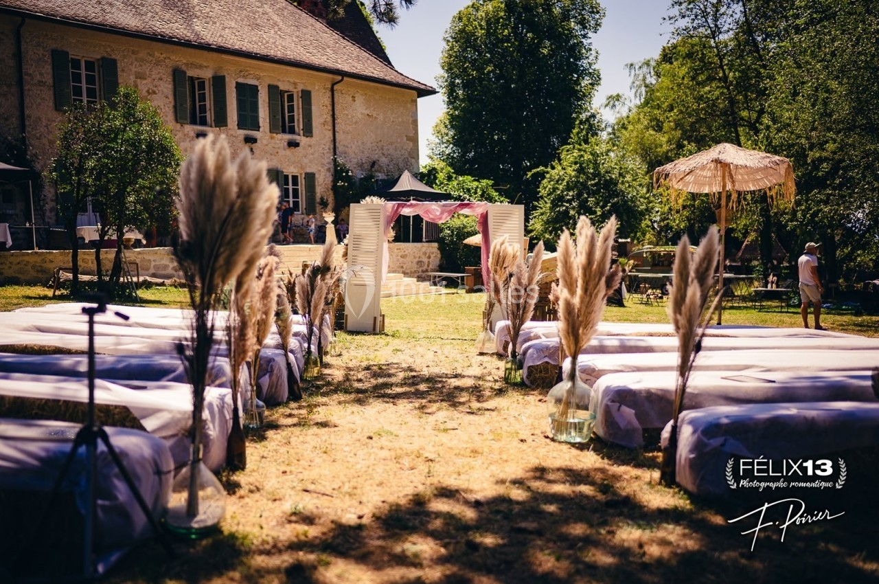 Allée décorée de bancs et de pampas menant à une arche de cérémonie en extérieur devant une maison ancienne.
