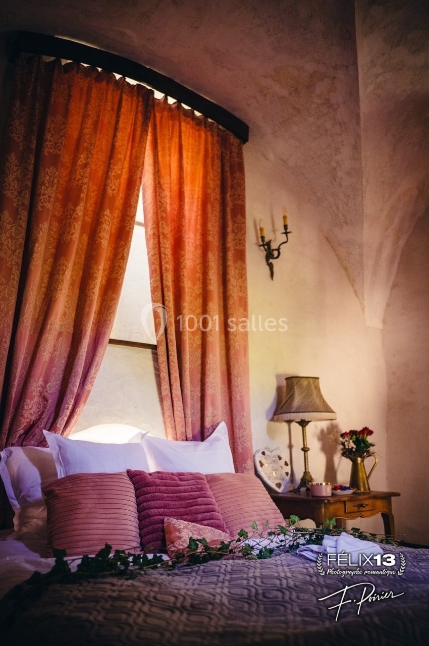 Lit avec coussins roses, drapé de rideaux orangés, éclairé par une lampe et décoré de fleurs dans une chambre chaleureuse.