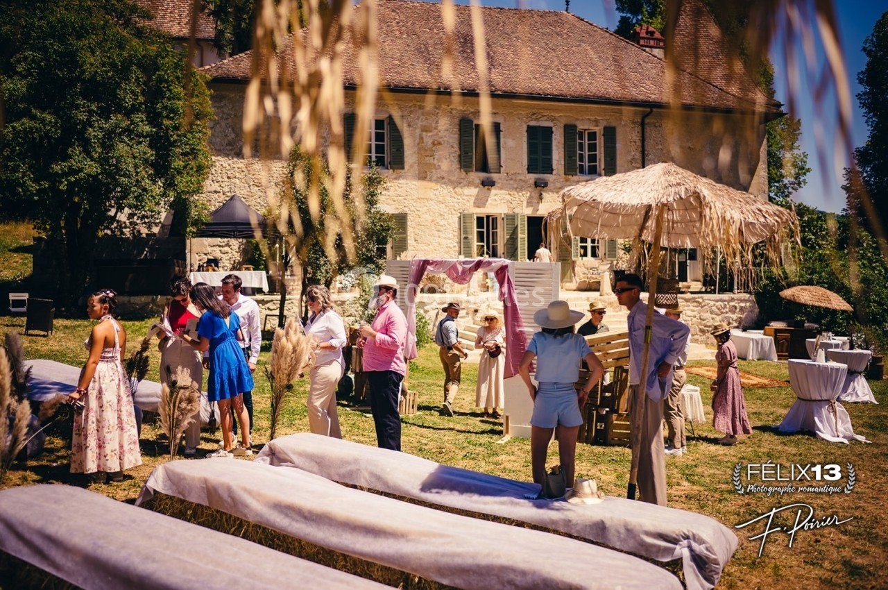 Groupe de personnes discutant dans un jardin devant une maison en pierre, décoré pour un événement en plein air.