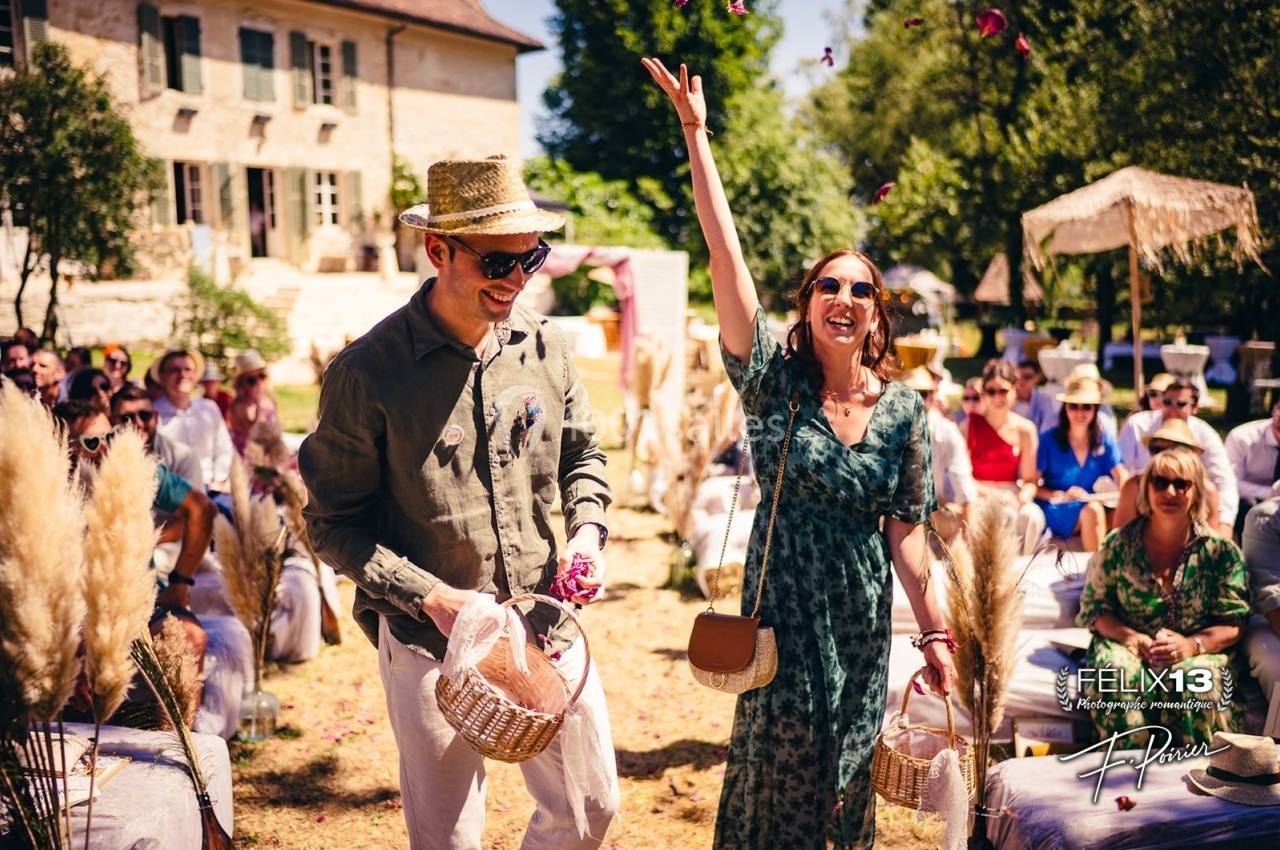 Un couple souriant lance des pétales de fleurs lors d'une cérémonie en plein air, entouré d'invités assis.