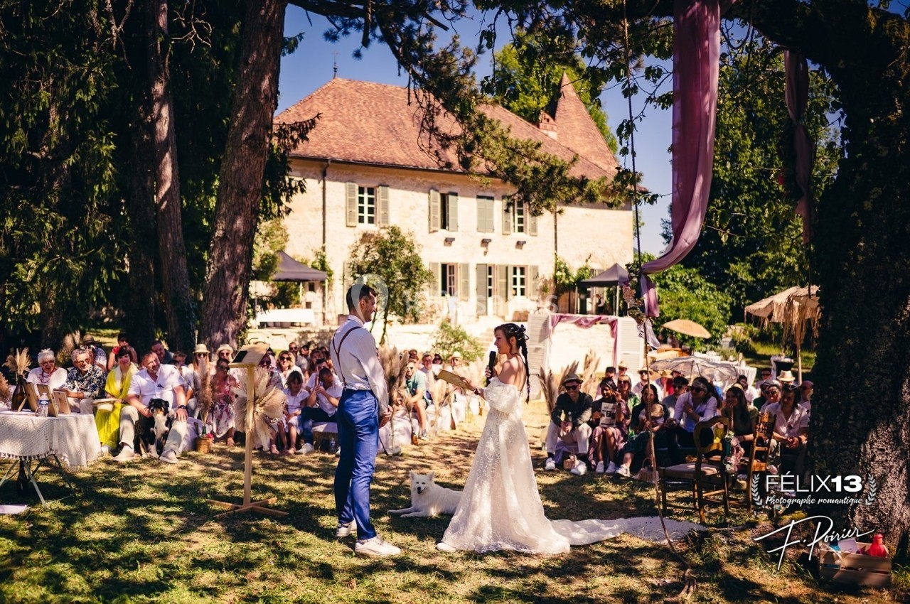 Un couple échange ses vœux lors d'une cérémonie de mariage en plein air, entouré d'invités sous des arbres.