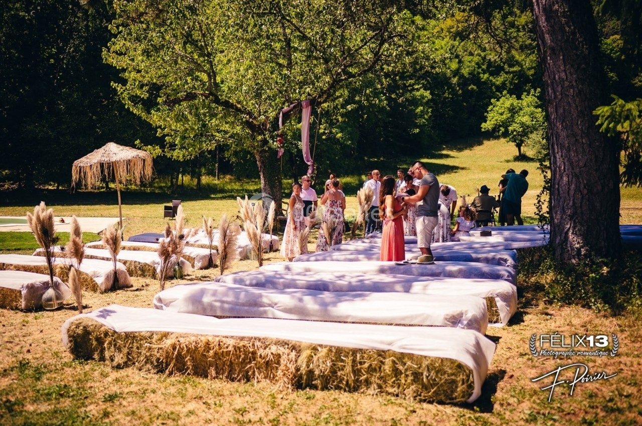 Des bancs en bottes de paille recouverts de tissu blanc disposés en extérieur pour une cérémonie champêtre.
