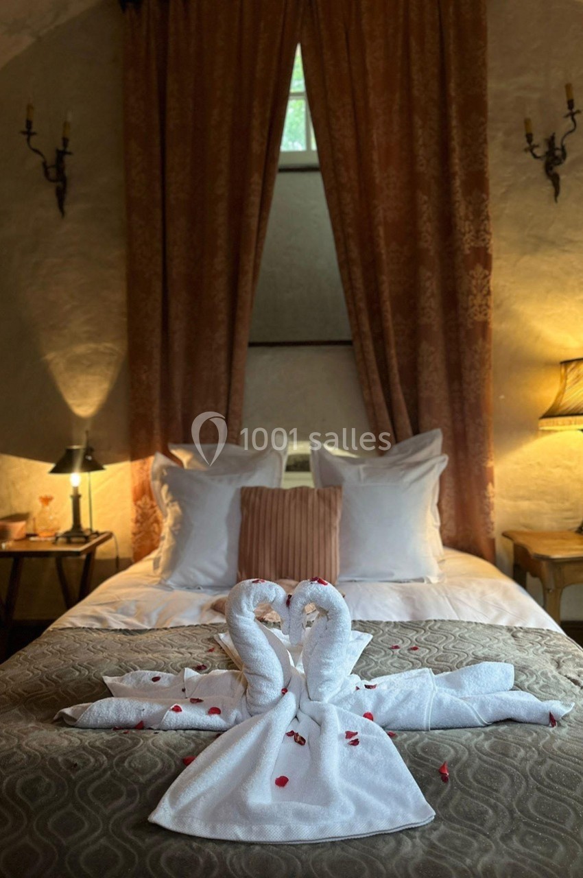 Lit décoré avec des serviettes en forme de cygnes et des pétales rouges, dans une chambre chaleureuse avec éclairage doux.