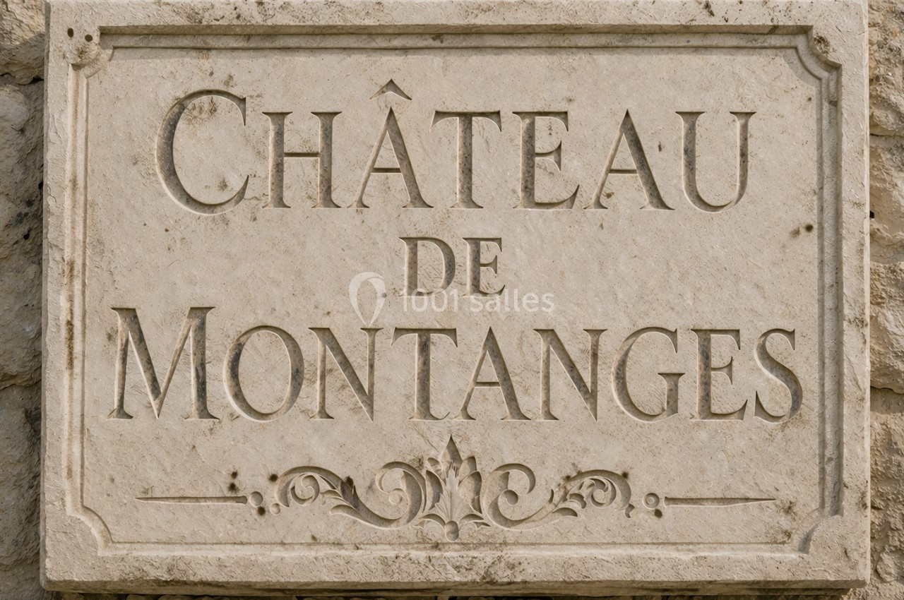 Plaque en pierre gravée indiquant ’Château de Montanges’, fixée sur un mur en pierre.