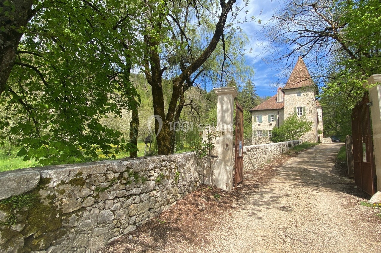 Entrée d'une propriété avec un chemin bordé de murs en pierre, menant à une maison ancienne entourée d'arbres.