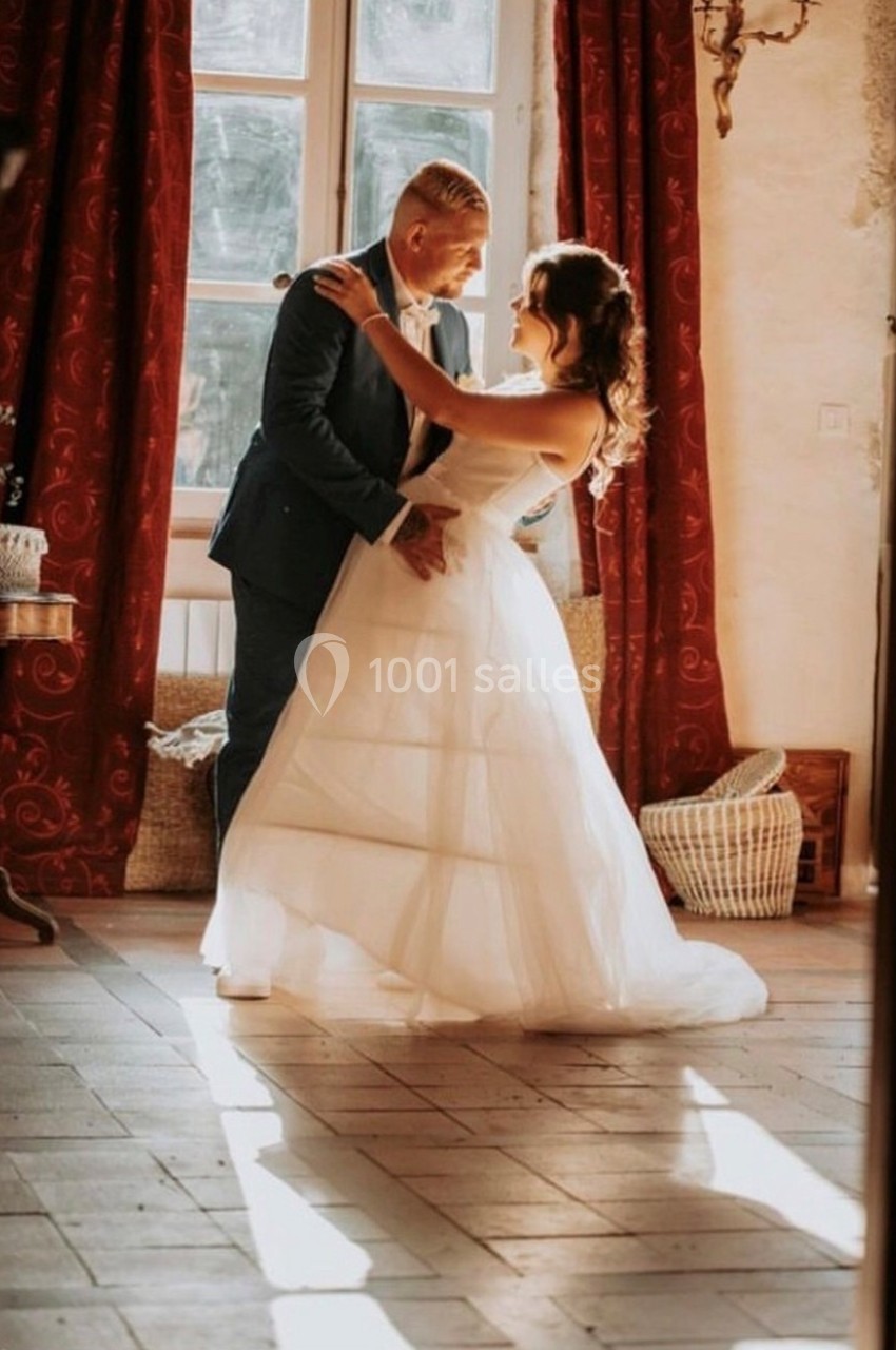 Un couple danse dans une pièce lumineuse avec des rideaux rouges et un sol en carreaux clairs.