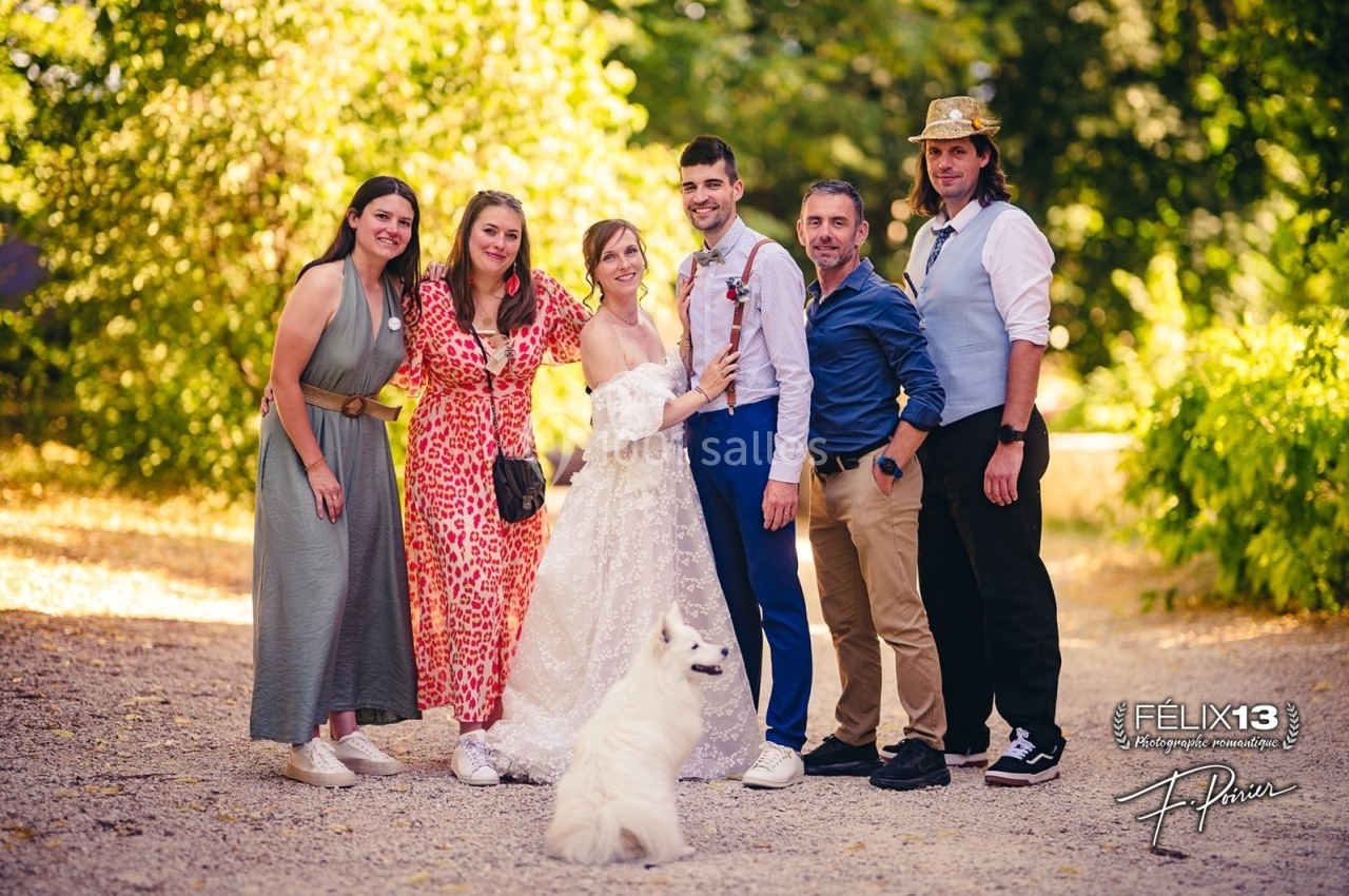 Un groupe de six personnes posant dehors avec un chien blanc au premier plan, entourés de verdure.