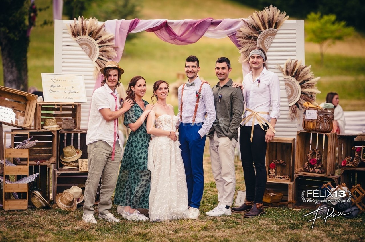 Un groupe de personnes posant devant une arche décorée de fleurs séchées dans un cadre champêtre.