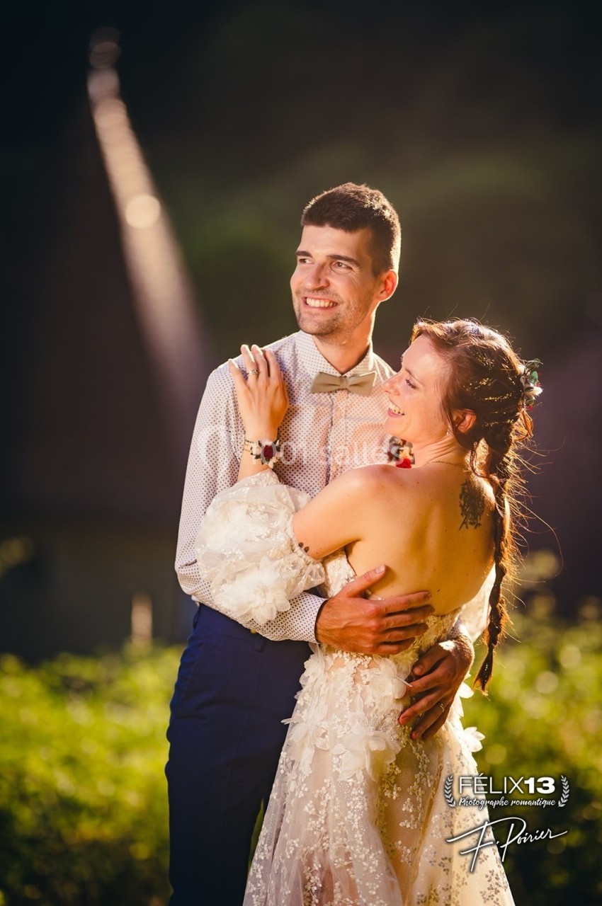 Un couple souriant en tenue de mariage, enlacé dans un cadre extérieur avec une lumière douce en arrière-plan.
