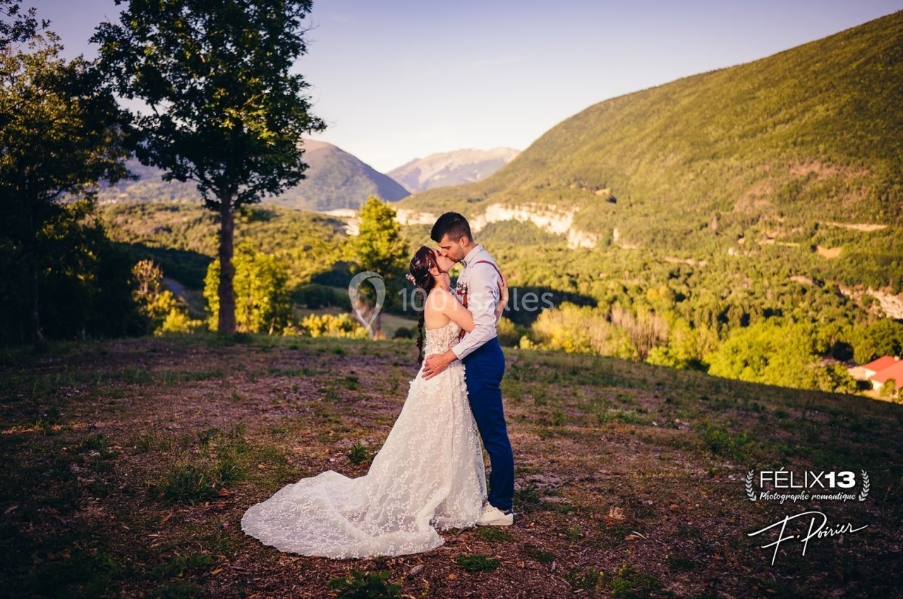 Un couple en tenue de mariage s'embrasse dans un paysage de montagne verdoyant sous un ciel dégagé.