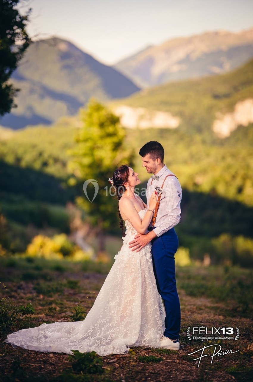 Un couple en tenue de mariage se tient tendrement dans un paysage naturel avec des montagnes en arrière-plan.