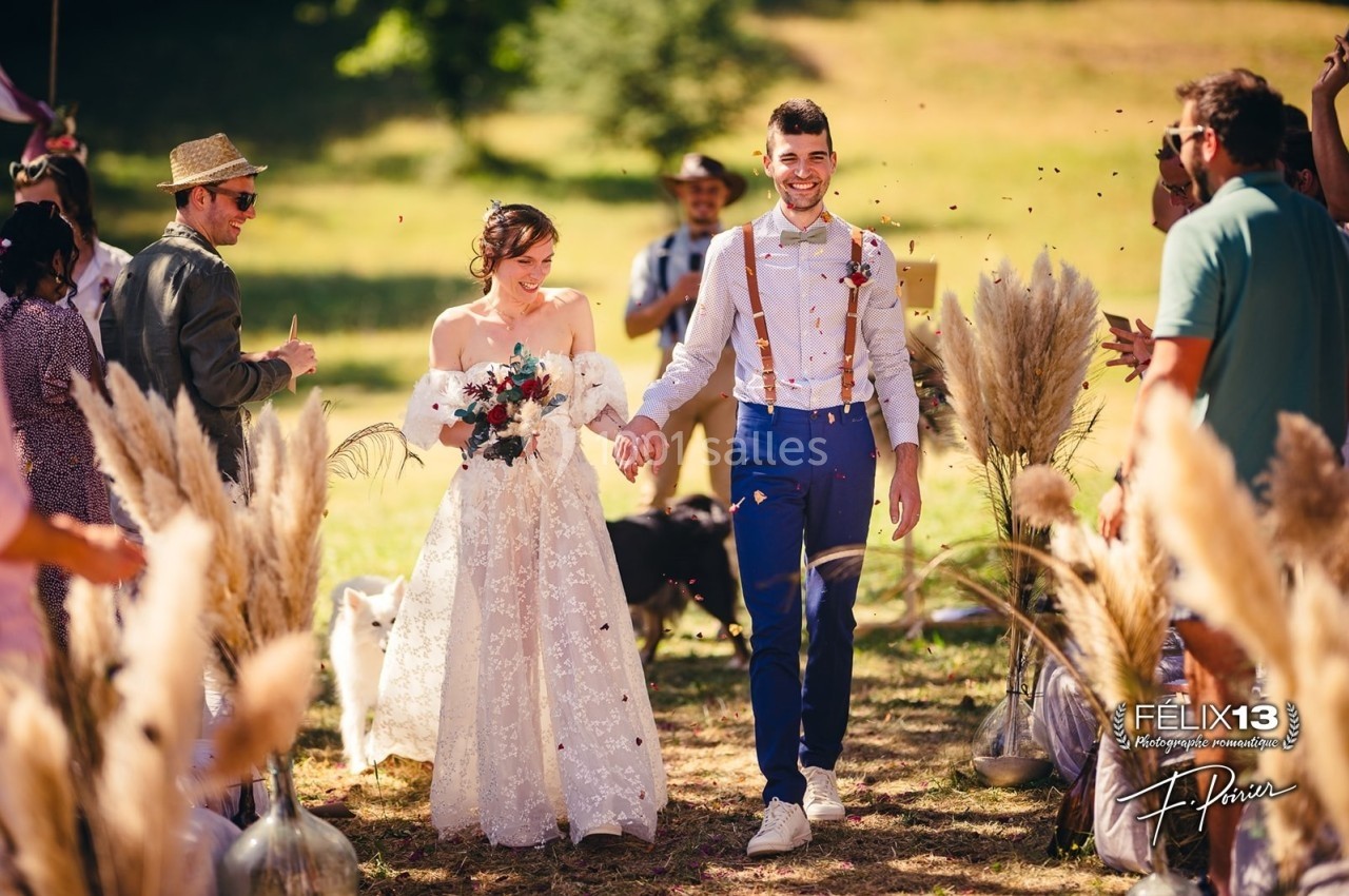 Un couple souriant marche main dans la main lors d'une cérémonie en plein air, entouré d'invités et de décorations…