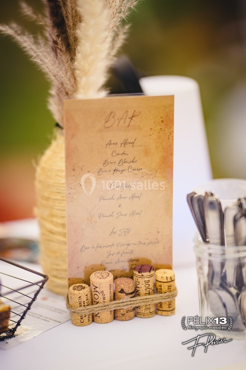 Carte de bar en papier beige avec une liste de boissons, décorée de bouchons de liège et d'herbes sèches.