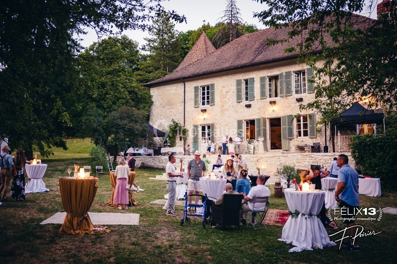 Personnes rassemblées dans un jardin devant une grande maison en pierre, lors d'une réception en plein air.
