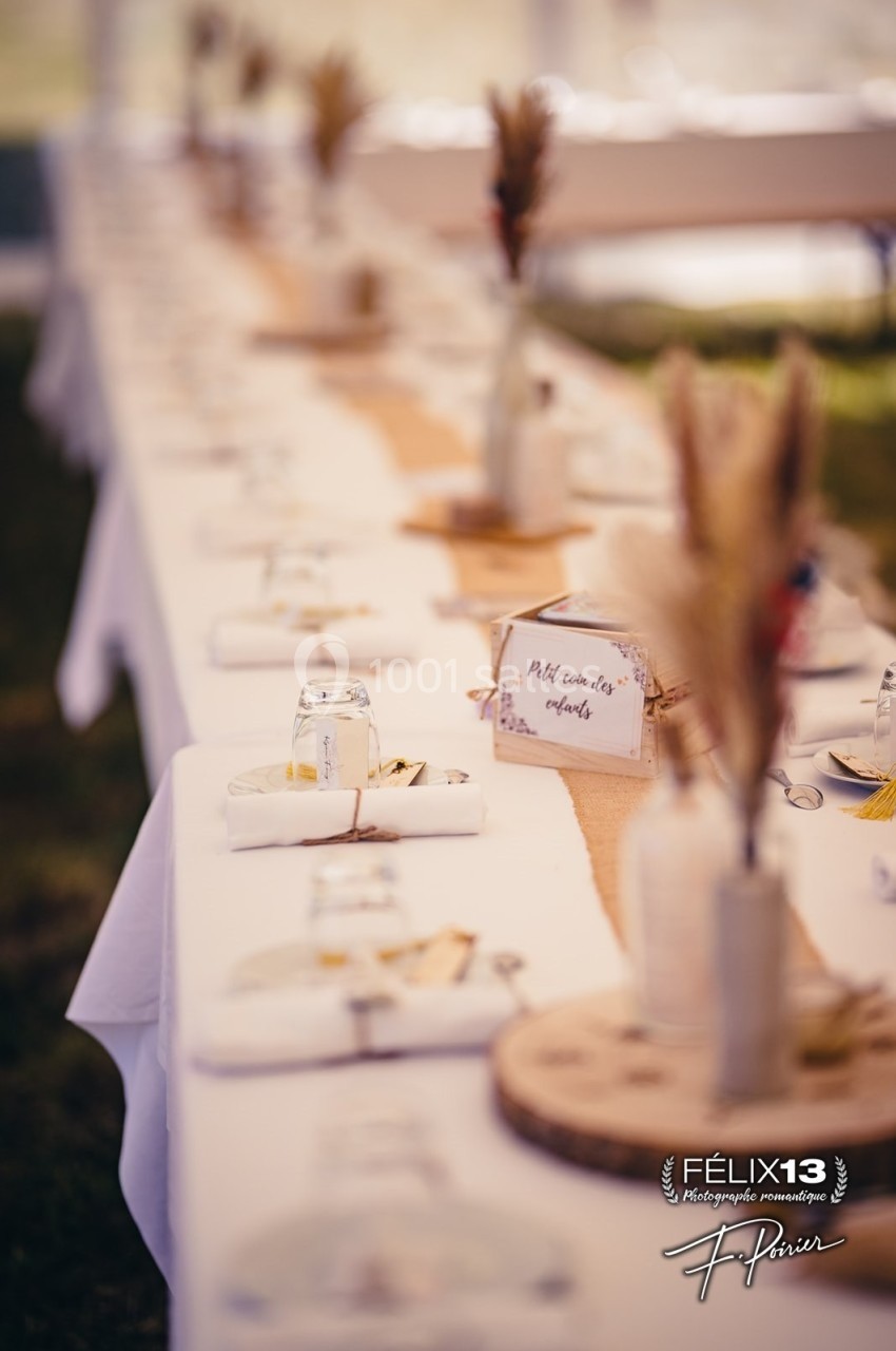 Table dressée pour un événement, avec nappes blanches, décorations rustiques et marque-places en bois et fleurs séchées.