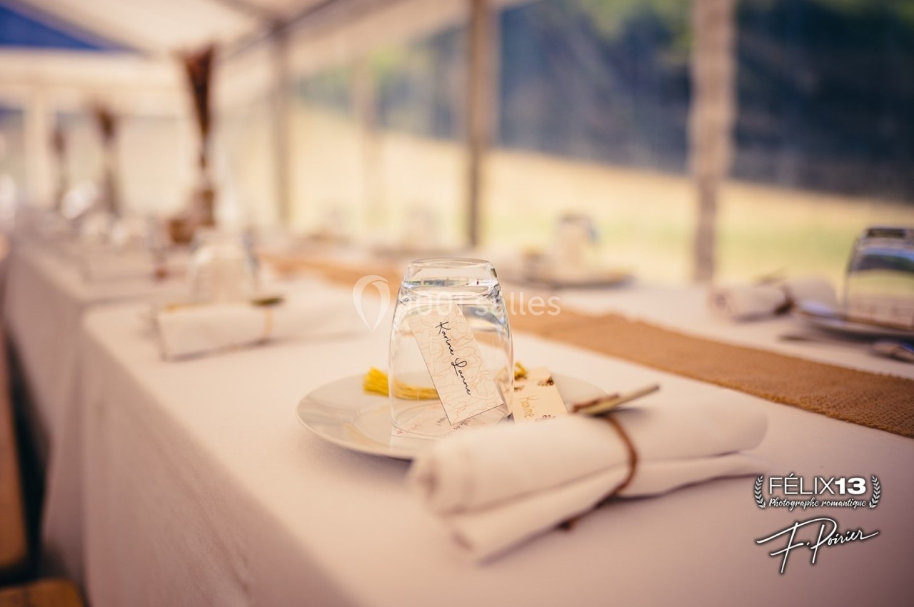 Verres retournés et serviettes pliées disposés sur une table dressée avec une nappe blanche et un chemin de table beige.