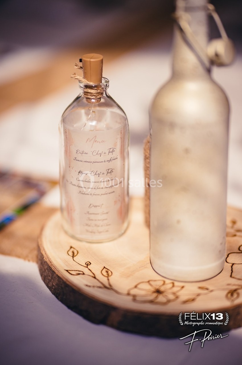 Deux bouteilles en verre, dont une avec un menu imprimé, posées sur une rondelle de bois gravée.