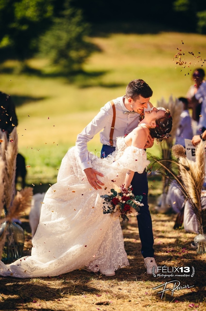 Un couple de mariés danse en extérieur, entouré de décorations champêtres et de pétales en suspension.