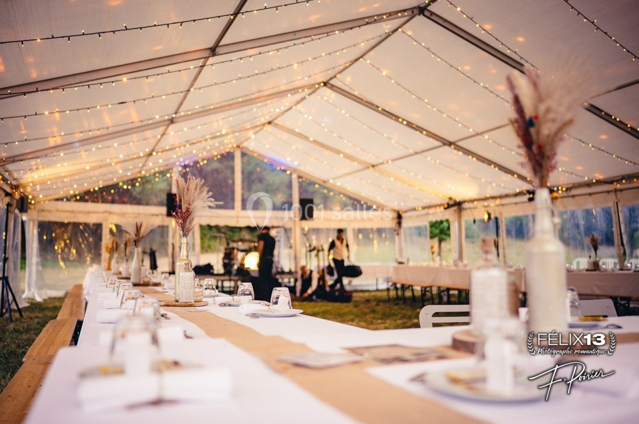 Intérieur d'une tente de réception avec tables décorées et guirlandes lumineuses suspendues.